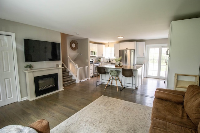 living room with dark wood-style flooring, a glass covered fireplace, and stairway