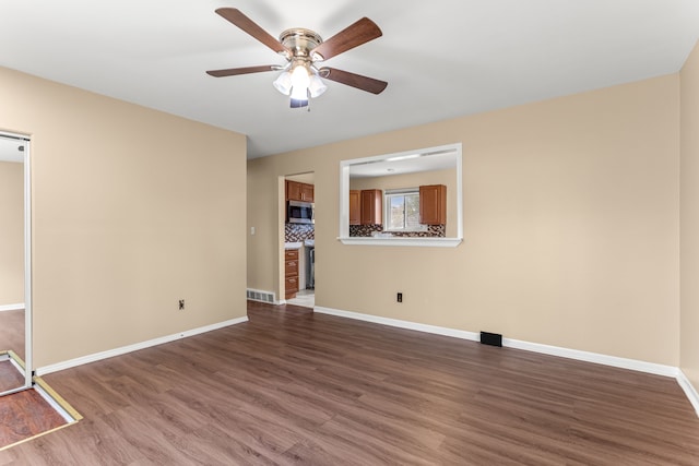 spare room with baseboards, ceiling fan, dark wood-style floors, and visible vents