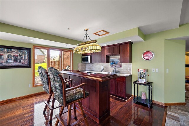 kitchen featuring a kitchen island, stainless steel microwave, baseboards, and dark wood-type flooring
