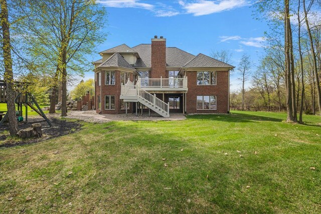 back of house featuring a deck, a chimney, brick siding, a yard, and stairway
