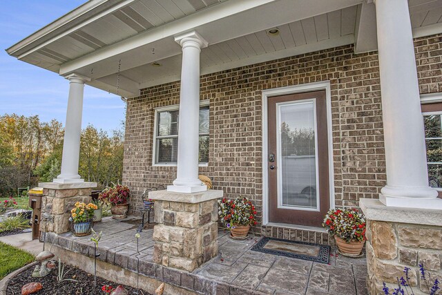 doorway to property featuring a porch and brick siding