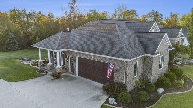 view of side of home featuring a shingled roof, an attached garage, brick siding, a yard, and driveway