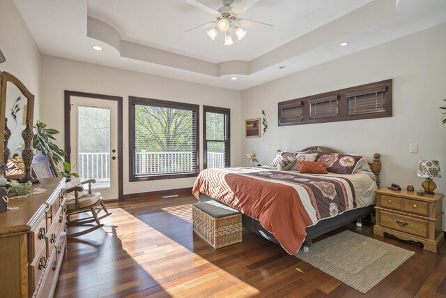 bedroom with access to outside, wood finished floors, a tray ceiling, and multiple windows