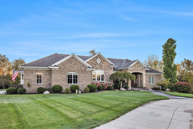 ranch-style home with brick siding, a shingled roof, and a front lawn