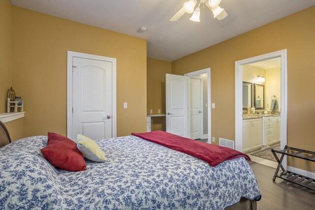 bedroom with a ceiling fan, visible vents, wood finished floors, baseboards, and connected bathroom