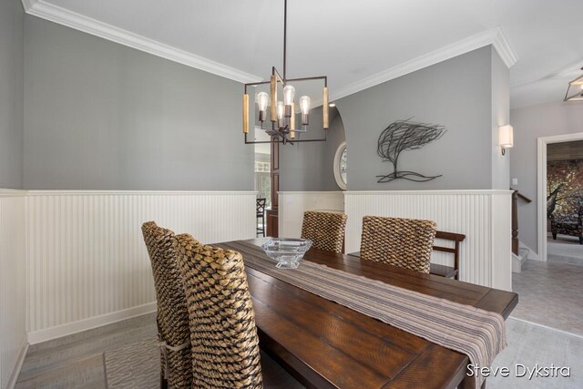 dining room featuring crown molding, wood finished floors, baseboards, a wainscoted wall, and a chandelier
