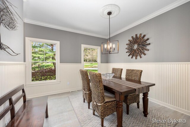dining space with crown molding, wainscoting, wood finished floors, and a notable chandelier