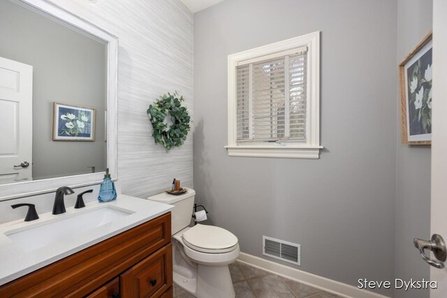 half bath with visible vents, tile patterned flooring, vanity, toilet, and baseboards