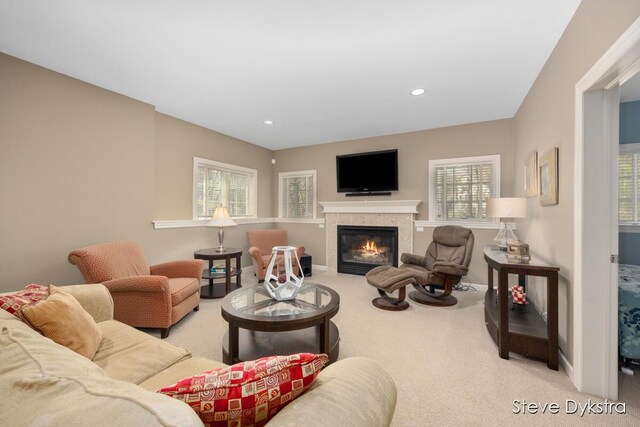living area with baseboards, a tiled fireplace, a healthy amount of sunlight, and carpet