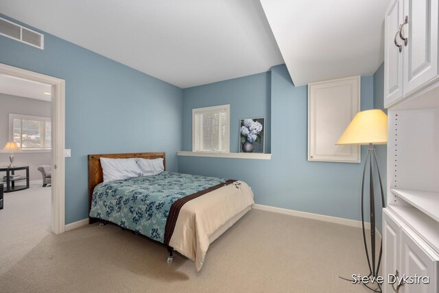 bedroom with baseboards, visible vents, and light carpet