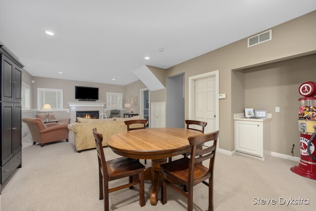 dining room featuring recessed lighting, light carpet, a warm lit fireplace, and visible vents