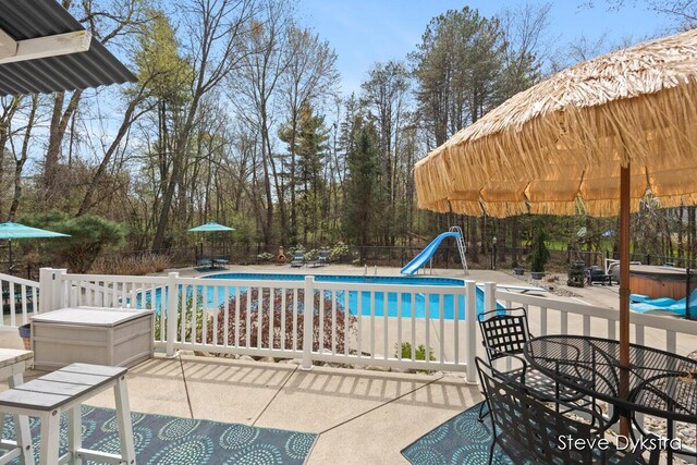 view of pool featuring a patio area, a hot tub, fence, a fenced in pool, and a water slide