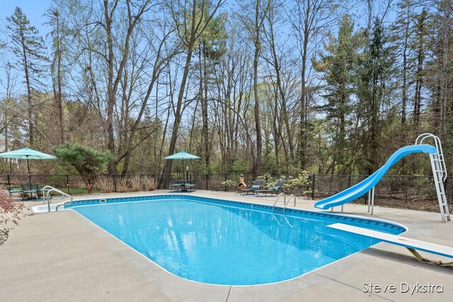 view of pool featuring fence, a diving board, a water slide, a fenced in pool, and a patio area