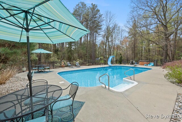 view of swimming pool featuring outdoor dining area, a patio area, fence, a fenced in pool, and a water slide