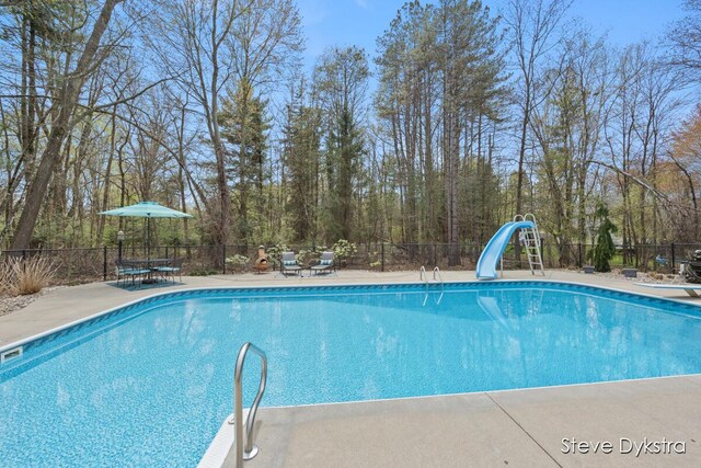 view of pool with a fenced in pool, a diving board, a water slide, and fence