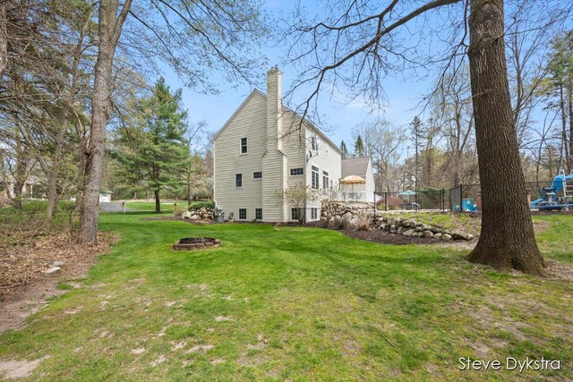 view of home's exterior featuring a lawn, a fire pit, fence, and a chimney
