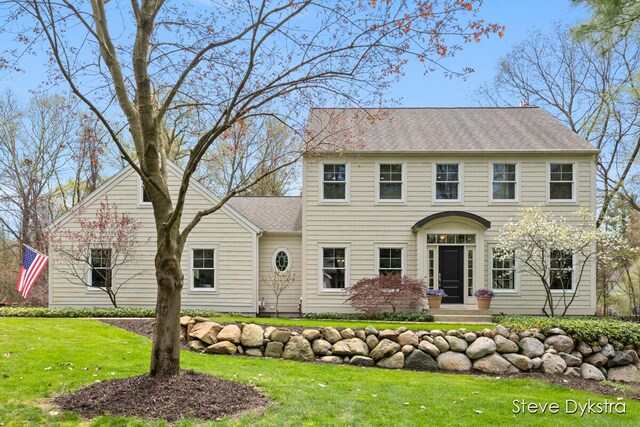 colonial-style house with a shingled roof and a front yard
