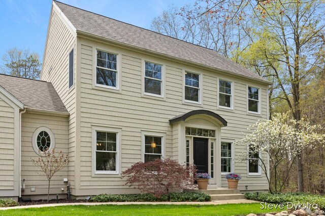 colonial inspired home featuring a shingled roof and a front lawn