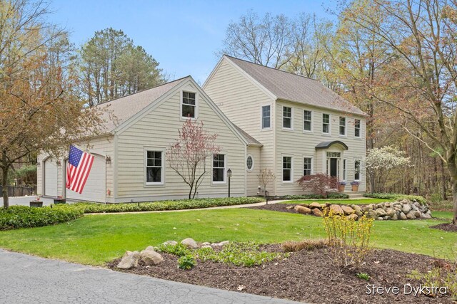 colonial-style house with roof with shingles, a front yard, and a garage