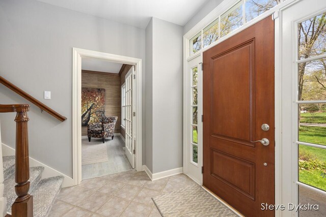 foyer entrance with stairway, light tile patterned floors, and baseboards