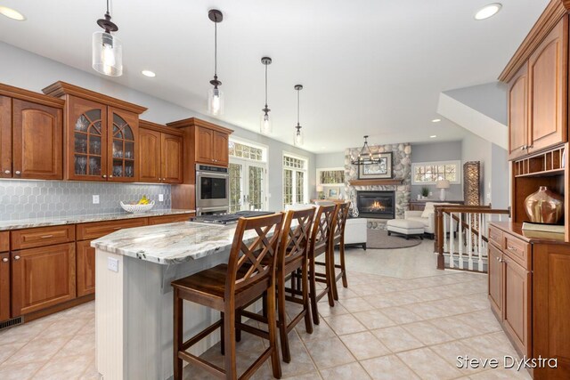 kitchen with a fireplace, light stone countertops, brown cabinets, open floor plan, and glass insert cabinets