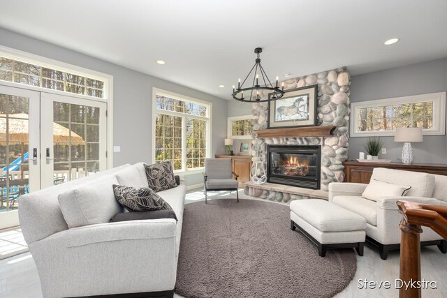 living area with a wealth of natural light, recessed lighting, a stone fireplace, and a chandelier