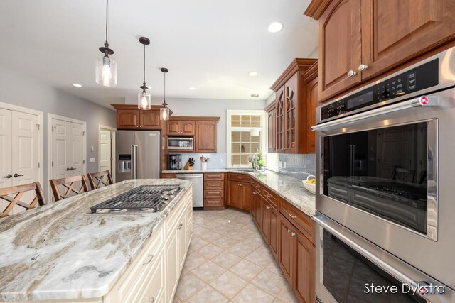 kitchen featuring brown cabinetry, a sink, light stone counters, glass insert cabinets, and stainless steel appliances