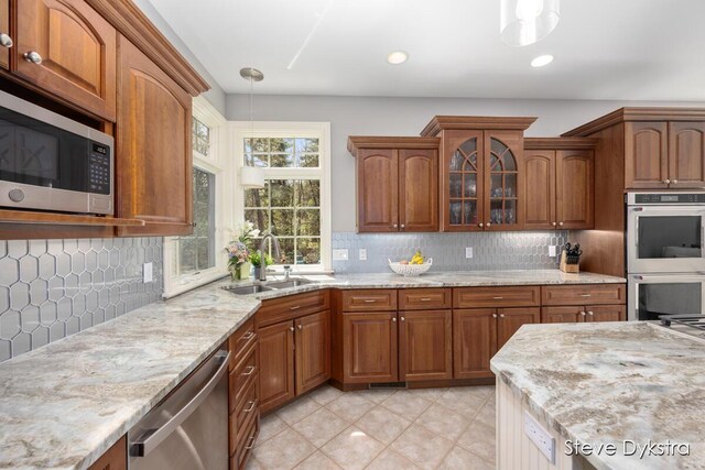 kitchen featuring hanging light fixtures, light stone countertops, a sink, glass insert cabinets, and stainless steel appliances