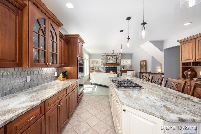 kitchen featuring light stone counters, a stone fireplace, open floor plan, tasteful backsplash, and glass insert cabinets