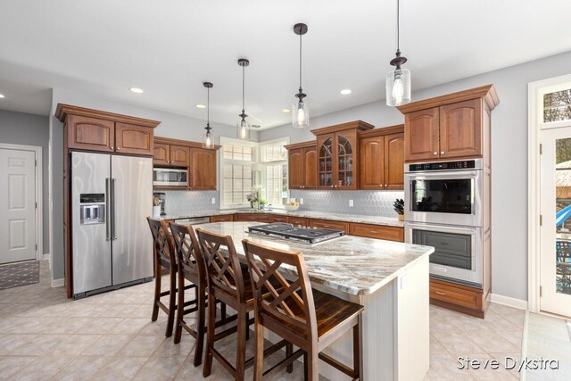 kitchen with a breakfast bar area, backsplash, stainless steel appliances, and brown cabinets