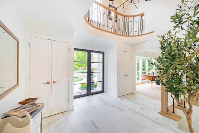 entryway with healthy amount of natural light, french doors, marble finish floors, a high ceiling, and a chandelier