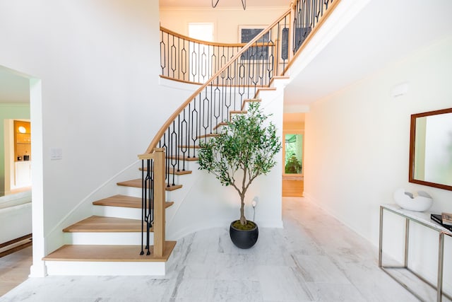 stairway featuring crown molding, a towering ceiling, marble finish floors, and baseboards