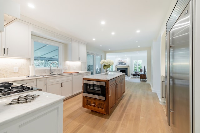 kitchen with built in appliances, a sink, backsplash, white cabinets, and recessed lighting