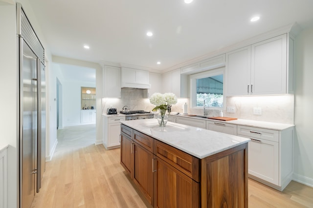 kitchen with stainless steel appliances, light wood-type flooring, a kitchen island, decorative backsplash, and white cabinets