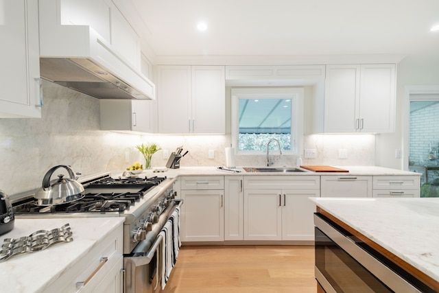 kitchen with stainless steel appliances, premium range hood, white cabinets, light wood finished floors, and recessed lighting