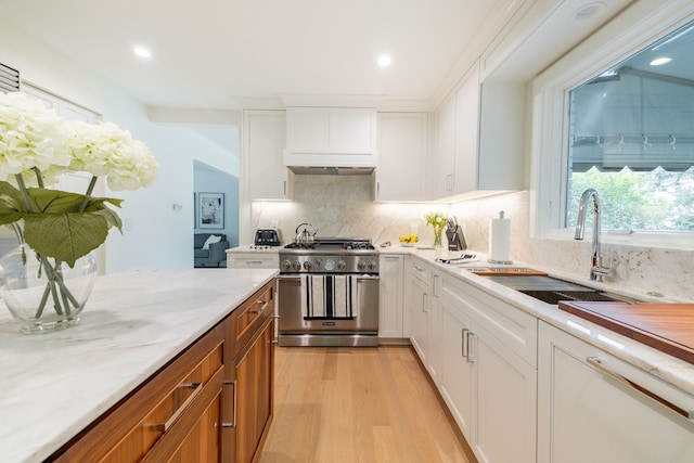 kitchen with stainless steel stove, a sink, light wood-type flooring, white cabinets, and backsplash