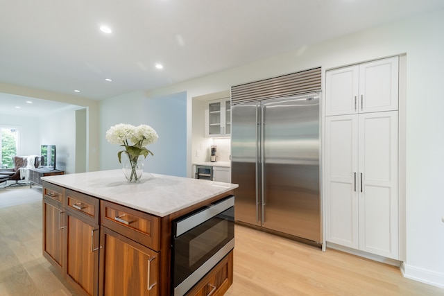kitchen featuring built in appliances, light wood-type flooring, a center island, white cabinetry, and recessed lighting