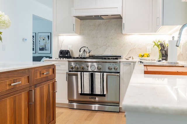 kitchen featuring high end stainless steel range, light countertops, white cabinetry, crown molding, and brown cabinetry