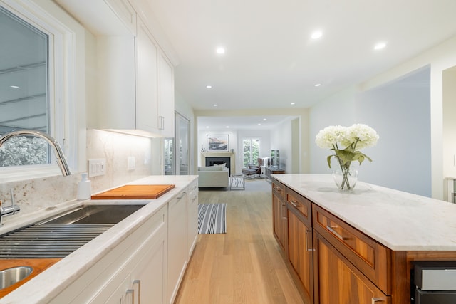 kitchen featuring a sink, light wood-type flooring, white cabinetry, recessed lighting, and light stone counters