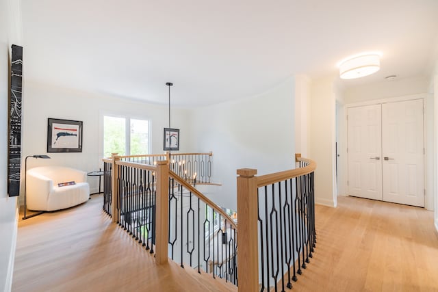 corridor with an upstairs landing, light wood-style flooring, ornamental molding, and baseboards