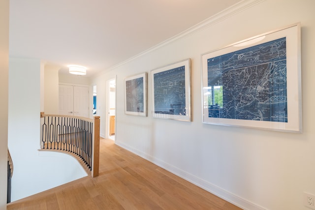 hallway with an upstairs landing, wood finished floors, baseboards, and crown molding