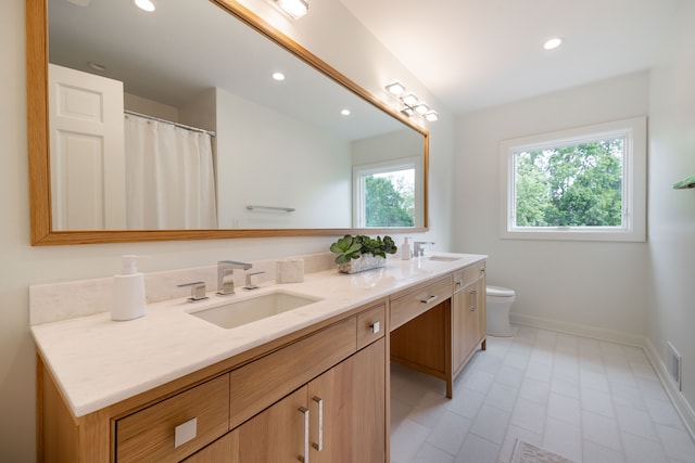 bathroom with baseboards, double vanity, toilet, and recessed lighting