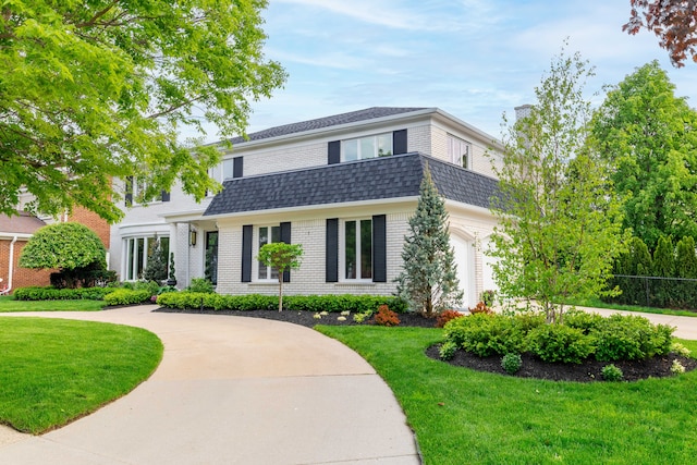 dutch colonial featuring a front lawn, roof with shingles, and brick siding