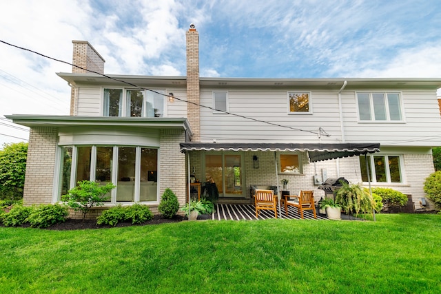 rear view of property featuring brick siding, a chimney, and a lawn