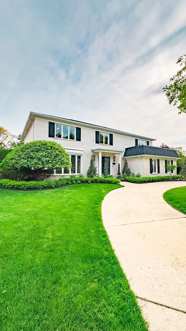 view of front facade with a front yard, brick siding, and curved driveway