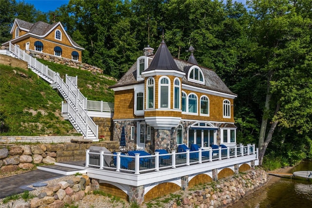 back of property featuring stone siding, a deck with water view, and stairway