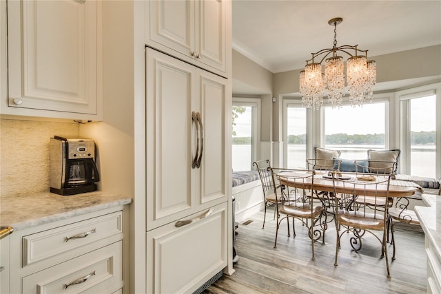 dining area featuring an inviting chandelier, a water view, ornamental molding, and wood finished floors