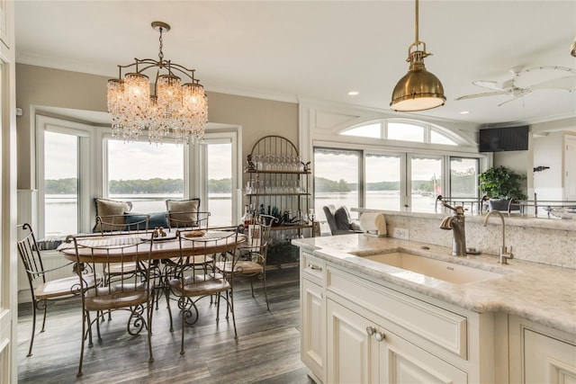 kitchen with light stone counters, a sink, dark wood finished floors, a wealth of natural light, and pendant lighting