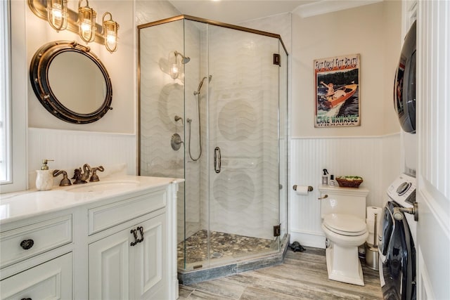 bathroom featuring wainscoting, stacked washing maching and dryer, wood finished floors, and toilet