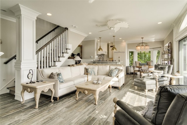 living room featuring light wood-style floors, stairs, crown molding, and ceiling fan with notable chandelier